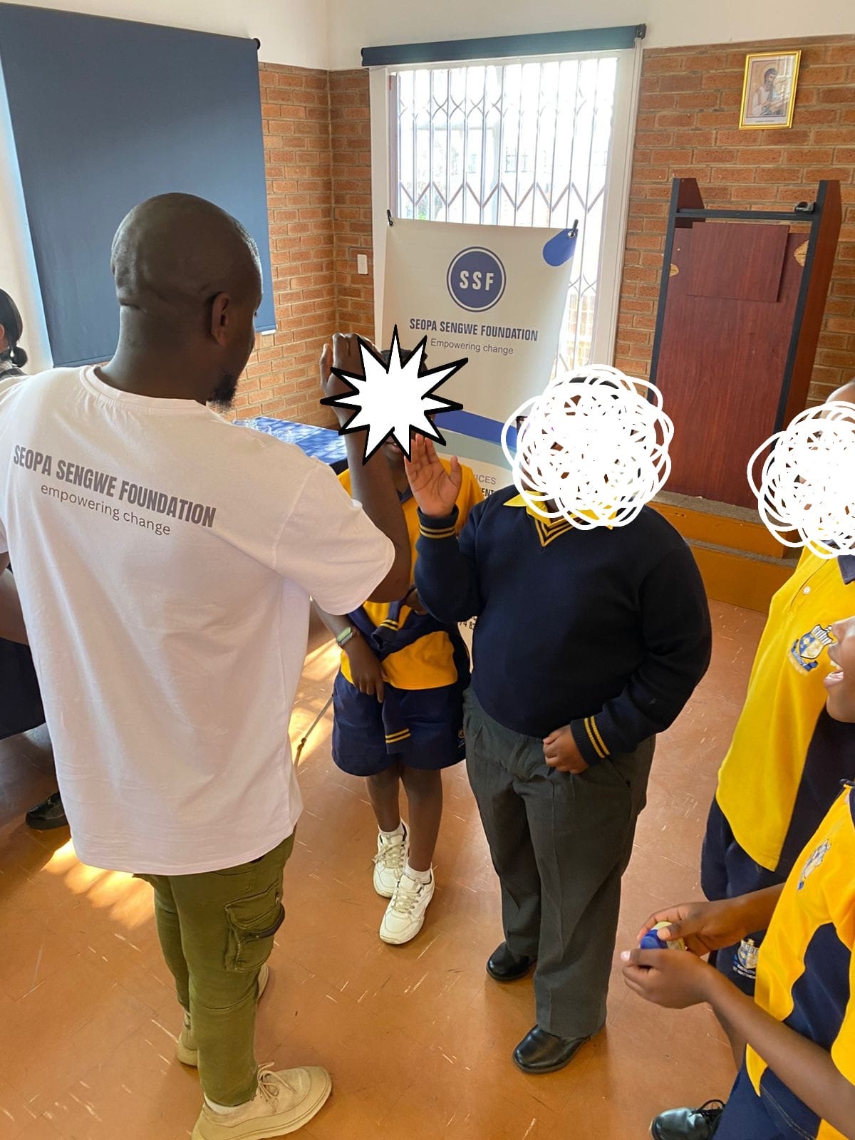 SSF facilitator greeting learners beside the foundation banner at a school hall